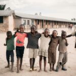 Group of happy children embracing each other in an African schoolyard setting.